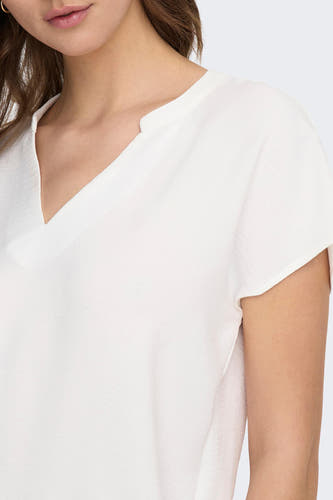 Chemisier blanc à manches courtes de JDY, vu de dos sur un mannequin portant un pantalon noir ample et des ballerines marron.