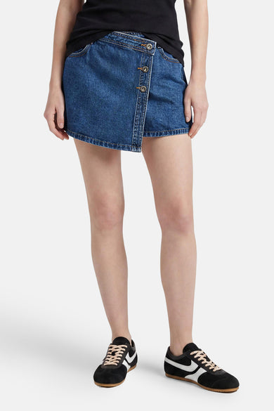 Donkerblauwe denim skort van ONLY met overslag en knoopsluiting aan de voorkant, gedragen met een zwart shirt en zwarte met witte sneakers.