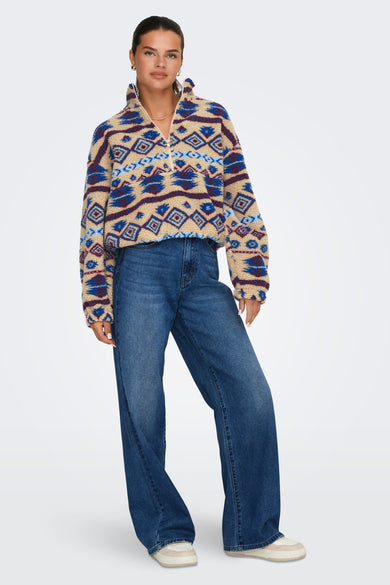 Beige fleece van ONLY met blauw en bordeauxrood patroon, gecombineerd met jeans en sneakers.
