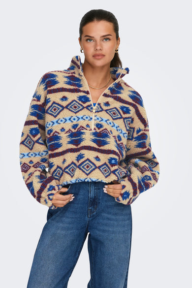 Beige fleece van ONLY met een kleurrijk geometrisch patroon, gecombineerd met een blauwe jeans en gouden sieraden.
