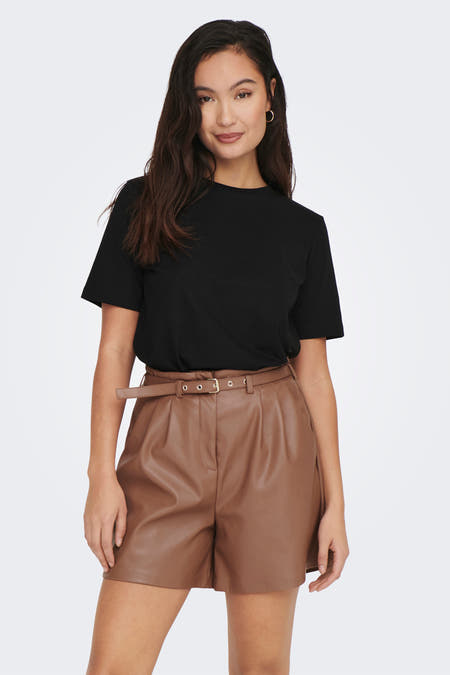 Zwart T-shirt van ONLY, gedragen met bruine leren shorts en gouden oorringen.