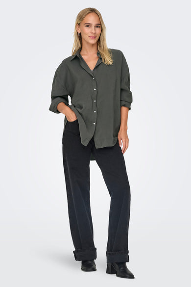 Grijs overhemd met lange mouwen van ONLY®, gedragen met zwarte jeans en laarzen met hak.
