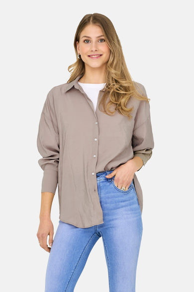 Beige hemd met lange mouwen van ONLY, gedragen over een wit T-shirt met blauwe jeans.

