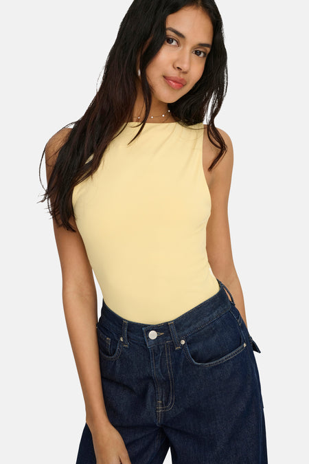 Haut jaune ONLY® à col montant, sans manches, porté avec un jean foncé.