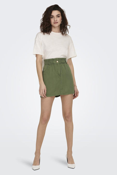 Groene korte rok van ONLY, gedragen met een wit T-shirt en witte pumps.
