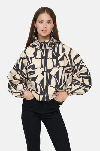 Korte beige jas van ONLY, met een abstract zwart patroon, gedragen met zwarte jeans en zilveren oorringen.
