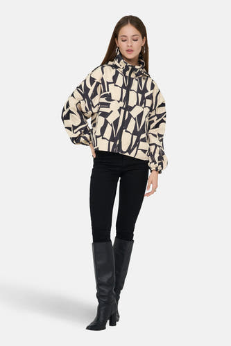 Beige korte jas van ONLY met een abstract zwart patroon, gedragen met zwarte broek en laarzen.