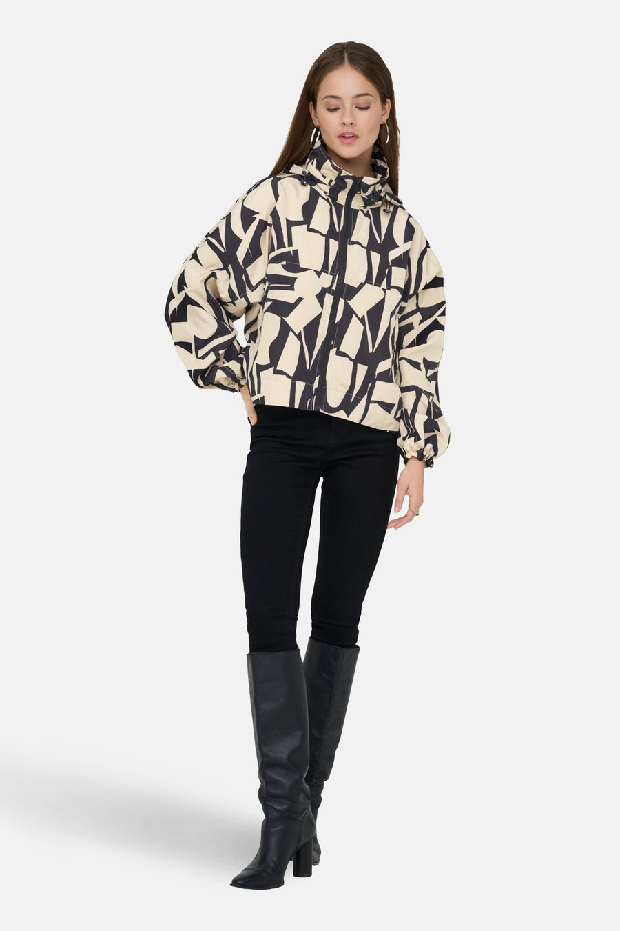 Beige korte jas van ONLY met een abstract zwart patroon, gedragen met zwarte broek en laarzen.