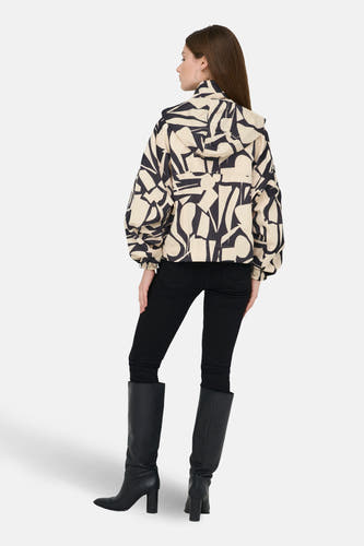Korte beige jas van ONLY, met een abstract zwart patroon, gecombineerd met zwarte broek en laarzen.