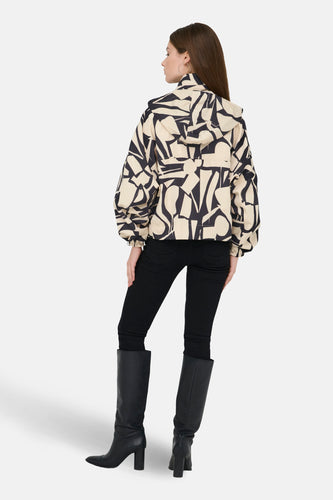 Korte beige jas van ONLY, met een abstract zwart patroon, gecombineerd met zwarte broek en laarzen.