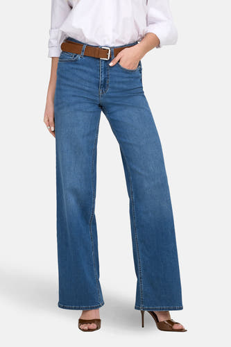 Wijdvallende jeans van ONLY, in blauw denim met bruine riem en witte blouse.
