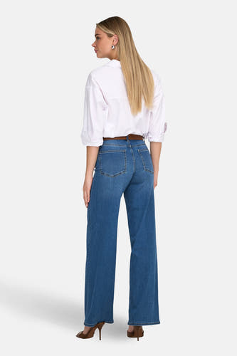 Wijd uitlopende jeans van ONLY®, in middenblauw denim, met een bruine riem en een wit overhemd.