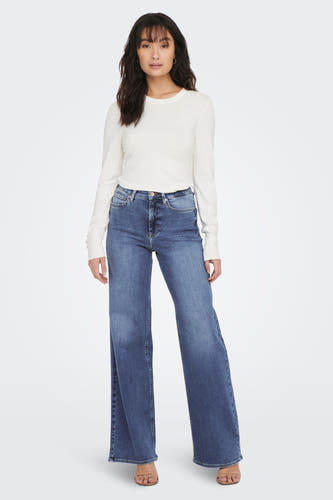 Jean large bleu de la marque ONLY®, combiné avec un chemisier blanc à manches longues et des sandales.