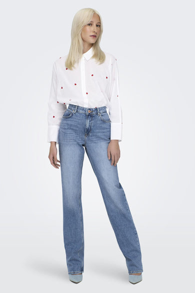 Wit hemd met lange mouwen van ONLY, met kleine rode hartjes, gecombineerd met blauwe jeans en hakken.
