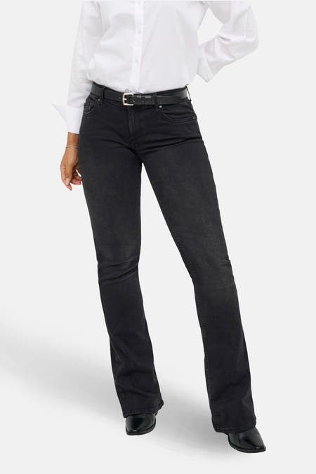 Jean flare noir de ONLY, avec une main dans la poche arrière et une blouse blanche.