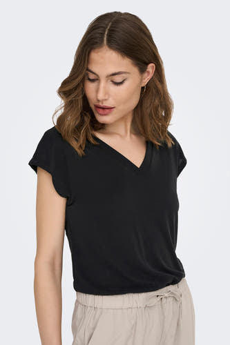 Zwart T-shirt met korte mouwen van ONLY, gedragen met een lichte broek en gouden oorbellen.