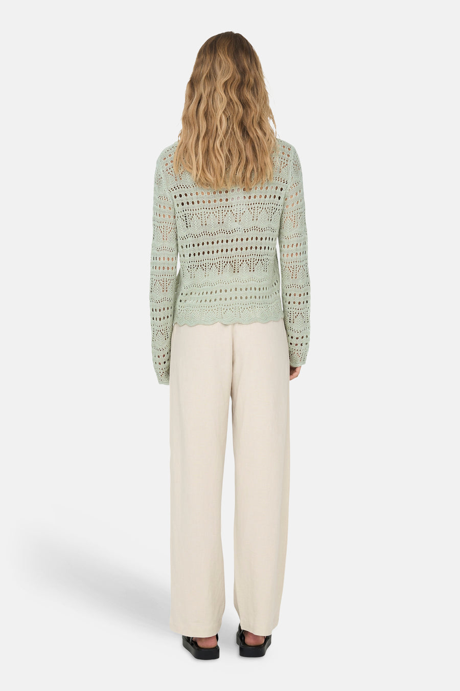 Groene ajourgebreide trui met ronde hals van JDY, met geschulpte zoom, gedragen met lichte broek en zwarte sandalen, van achteren gezien.