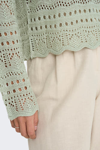 Groene trui met ronde hals van JDY, met een opengebreid patroon en beige broek.
