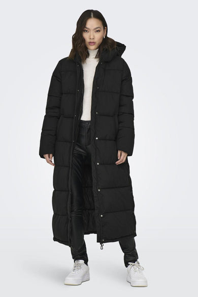 Manteau long noir ONLY, avec capuchon et fermeture à boutons, porté sur une veste blanche et un pantalon noir.