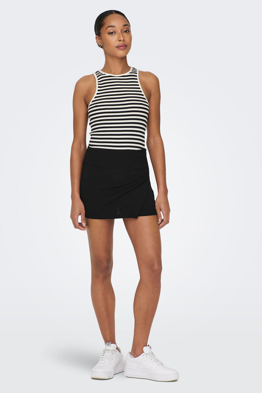 Zwarte skort van JDY met een overslagdetail, gecombineerd met een gestreepte top en witte sneakers.
