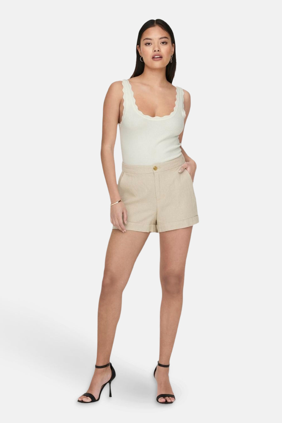 Witte mouwloze top van JDY met geschulpte rand en geribbelde stof, gedragen met beige shorts en zwarte hakken.