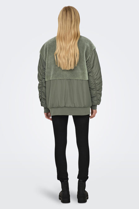 Groene jas van ONLY, met een teddy kraag en gerimpelde mouwen, gecombineerd met een zwarte broek en laarzen.

