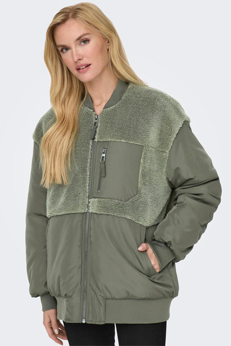 Groene lange jas van ONLY, met teddy accenten en een ritszak, gedragen door een blond model.

