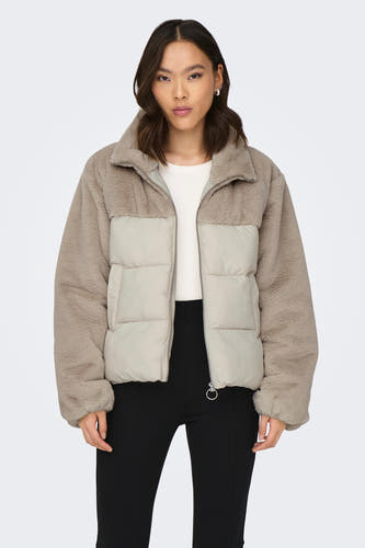 Kort ecru jasje van ONLY, met fleece en gewatteerd detail, gedragen over een witte trui en zwarte broek.

