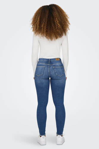 Jean skinny en denim de bleu, le 'BLUSH SKINNY' d'ONLY, porté par une femme en chemise blanche et des chaussures.