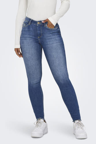 Jean skinny bleu d'ONLY, avec une main dans la poche et porté avec un t-shirt blanc.