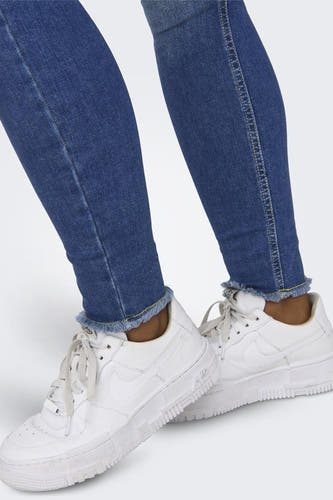Jean skinny bleu d'ONLY, avec un bord froncé et porté avec des baskets blanches.