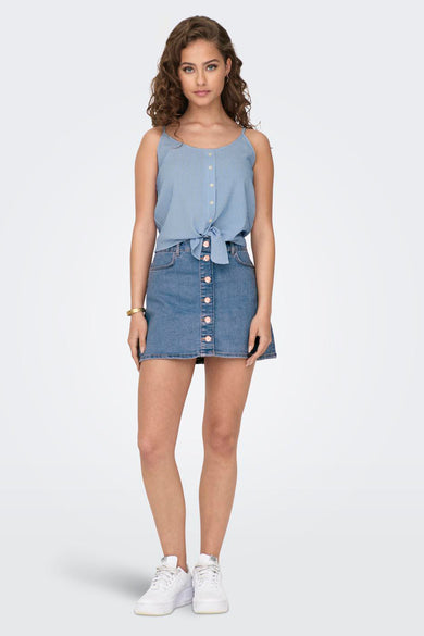 Blouse blanche sans manches de ONLY®, boutonnée à l'avant, associée à une jupe en denim et des baskets blanches.