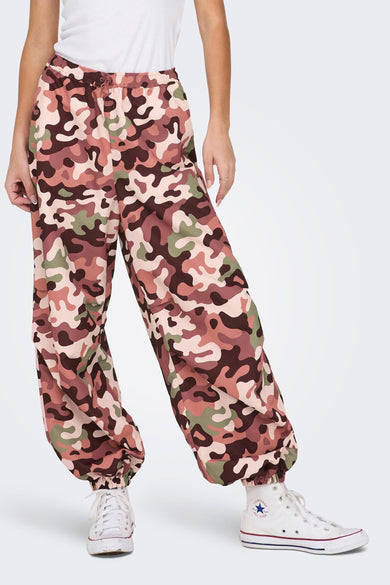 Camo broek van NEON & NYLON, met bruine en groene camouflageprint, gecombineerd met witte sneakers en een wit topje.
