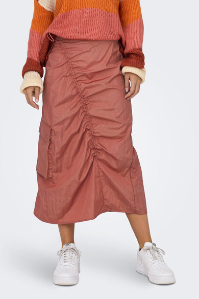 Roze rok van NEON & NYLON, met gedrapeerd detail en cargozak, gecombineerd met een gestreepte trui en witte sneakers.
