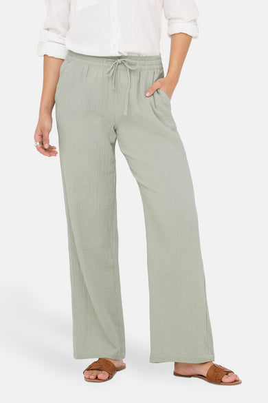 Groene broek van JDY, met trekkoord en zakken, gecombineerd met een wit overhemd en bruine sandalen.
