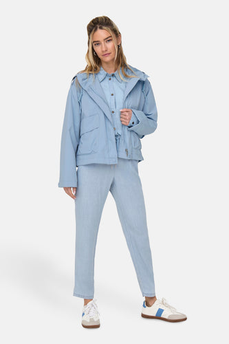 Vrouw draagt lichtblauwe outfit met jas, blouse, broek en witte sneakers.