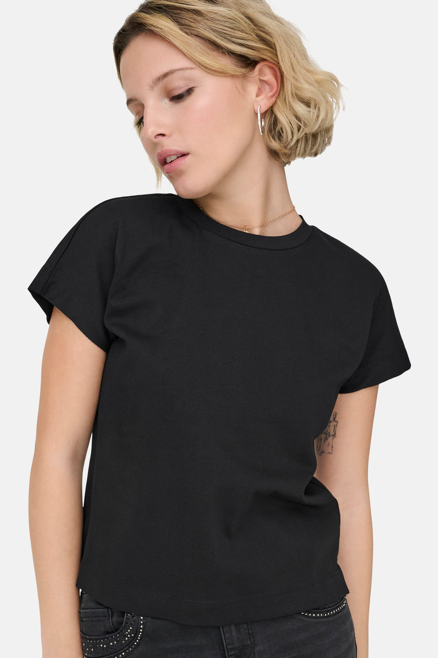 T-shirt noir à manches courtes de ONLY, avec un col rond et porté avec une chaîne dorée.