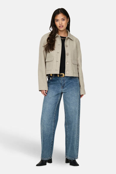 Beige korte jas van JDY, met lange mouwen en knoopsluiting, gecombineerd met een zwarte top en blauwe jeans.