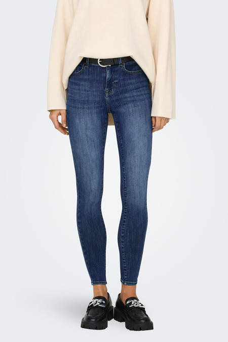 Donkerblauwe skinny jeans van ONLY, gedragen met een crèmekleurige trui, zwarte riem en loafers met kettingdetails.