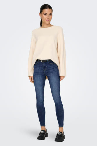 Donkerblauwe skinny jeans van ONLY®, gedragen door een model met een crèmekleurige trui, zwarte riem en grove zwarte instappers.