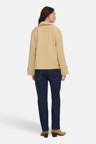 Manteau court beige de JDY, vu de derrière, avec des jeans bleu marine et des bottes en cuir.