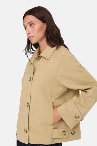 Dame met bruin haar in een zandkleurige jas met knopen.
