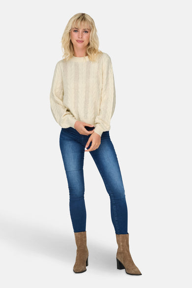 Witte trui met ronde hals van ONLY, met kabelpatroon en gedragen met jeans en laarzen.
