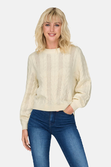 Witte trui met ronde hals van ONLY®, met kabelpatroon en blauwe jeans.

