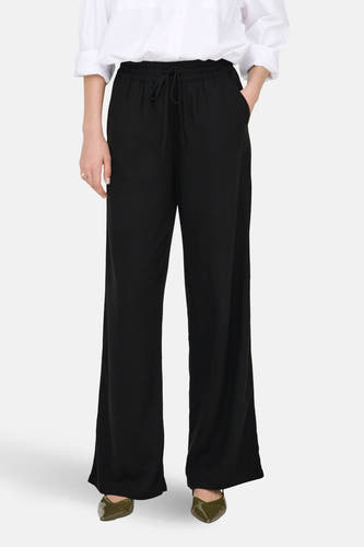 Zwarte broek van JDY, met een elastische tailleband en wijde pijpen, gecombineerd met een wit overhemd en groene schoenen.
