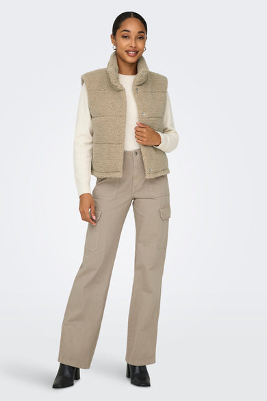 Bodywarmer teddy beige de la marque ONLY® avec boutons, porté sur un pull blanc et un pantalon cargo beige, vue de face.