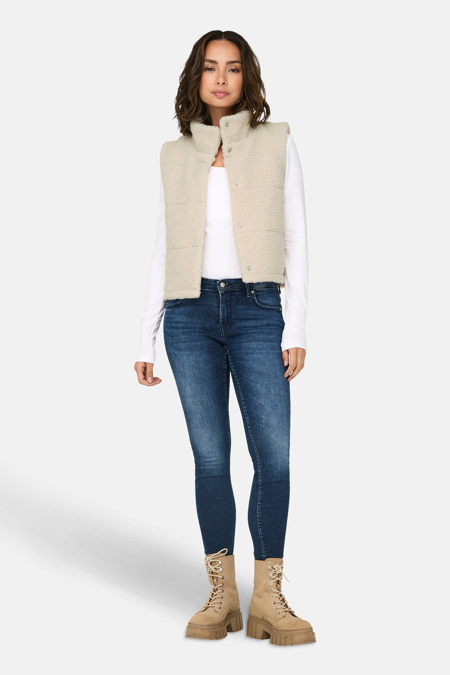 Ecru bodywarmer van ONLY, gedragen over een wit shirt met lange mouwen en donkere jeans, gecombineerd met beige laarzen.
