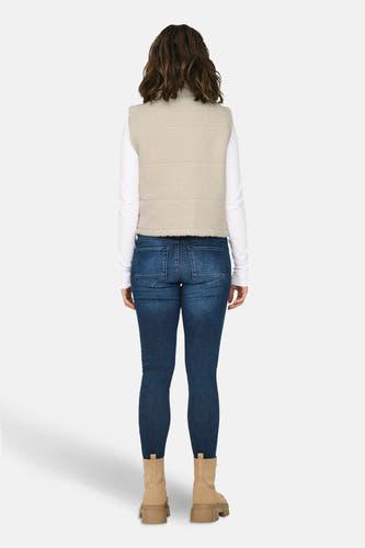 Ecru bodywarmer van ONLY, met wafeltextuur, gedragen over een wit shirt en donkere jeans met beige laarzen, achteraanzicht.
