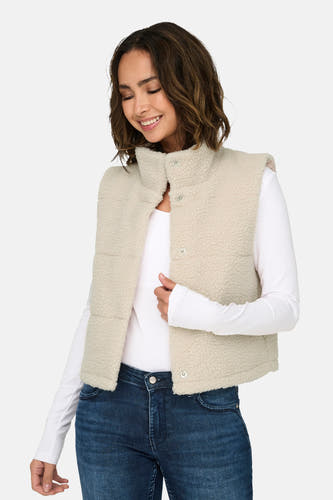 Ecru bodywarmer van ONLY, met drukknopen en een kraag, gecombineerd met een wit shirt met lange mouwen en een donkere jeans.
