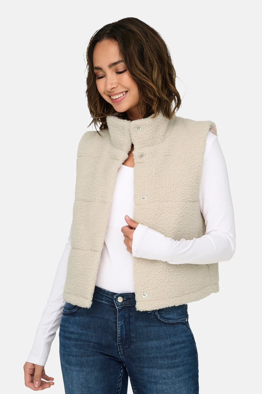 Ecru bodywarmer van ONLY, met drukknopen en een kraag, gecombineerd met een wit shirt met lange mouwen en een donkere jeans.

